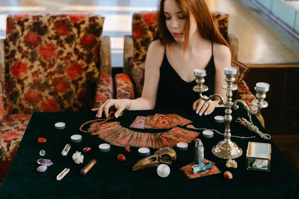 A tarot reader seated at a velvet-covered table with cards fanned out, candles, crystals and a candelabra