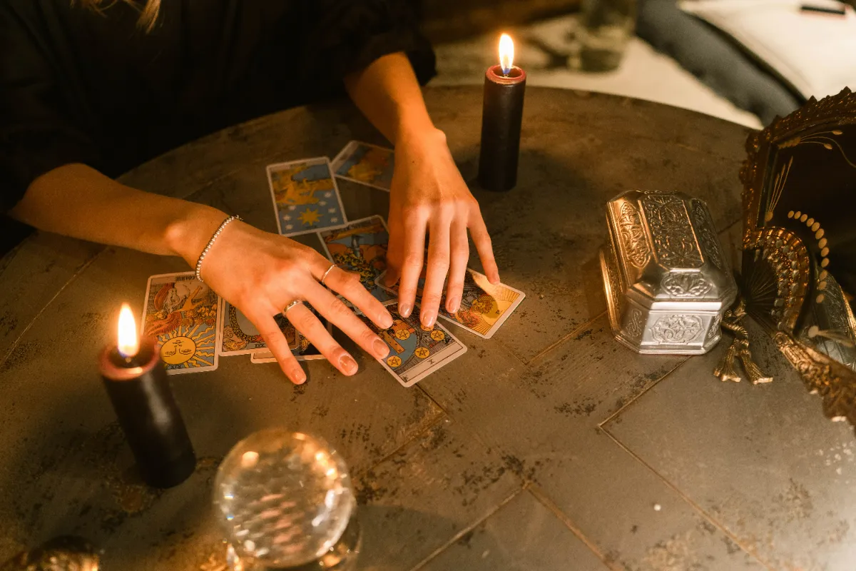 A reader laying out tarot cards by candlelight beside a crystal ball on a round table